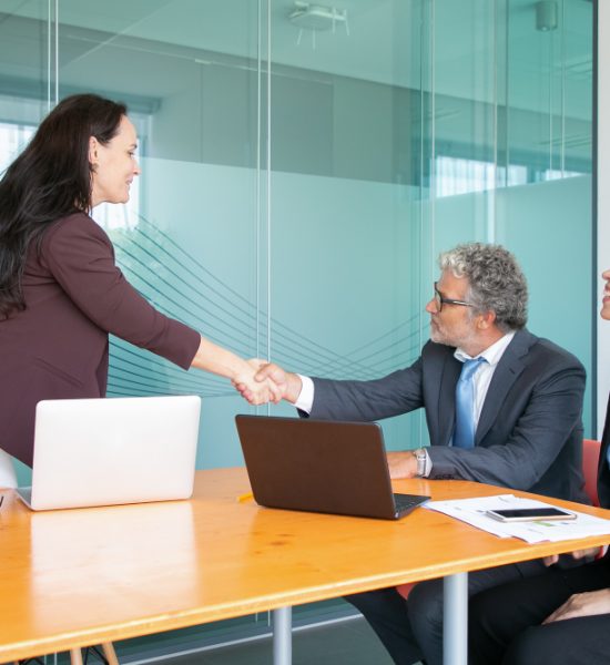 experienced-grey-haired-ceo-sitting-greeting-businesswoman